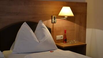 Une chambre d’hôtel avec une tête de lit en bois, deux oreillers blancs, une table de chevet avec une lampe, une bouteille et un verre.