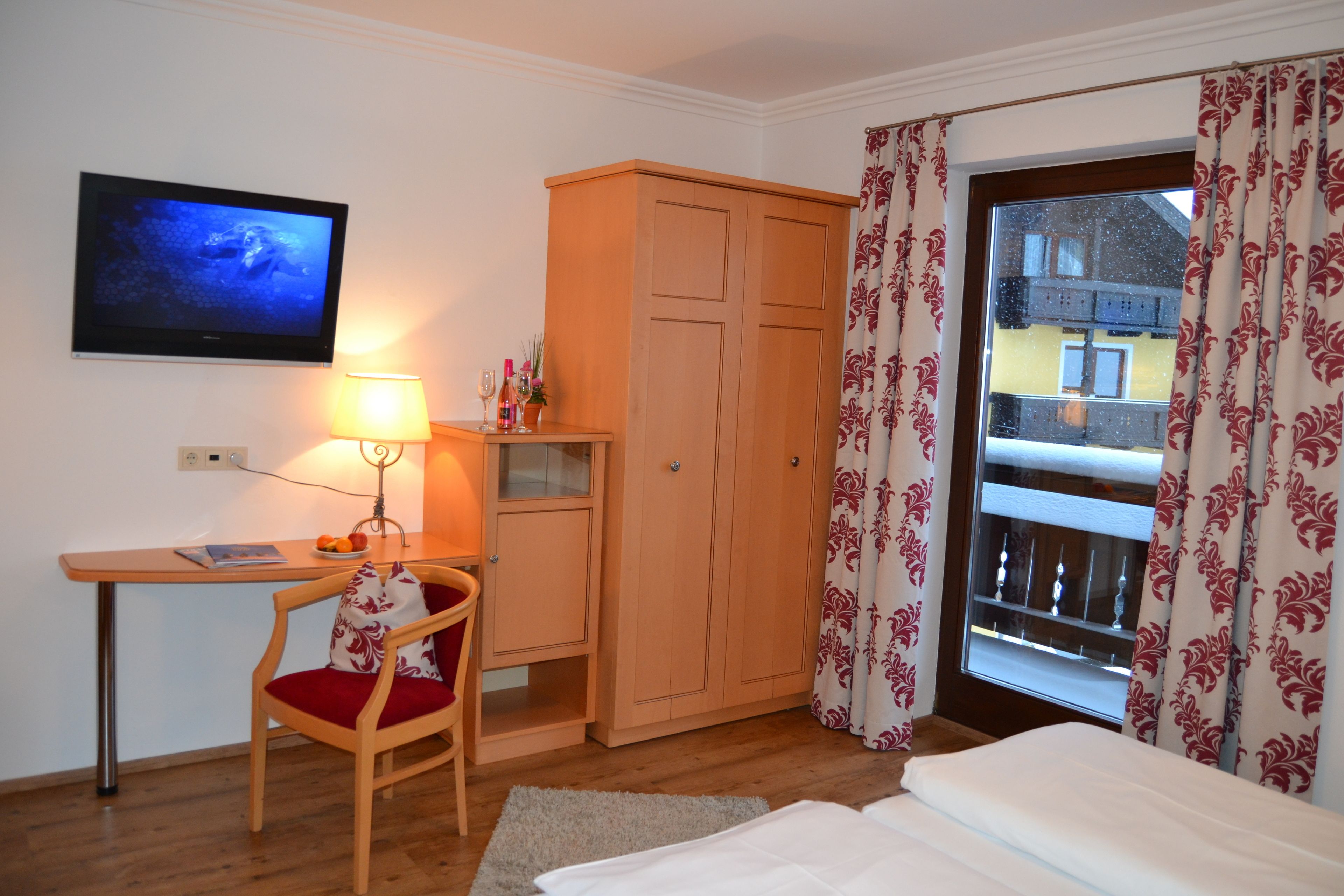 Ett hotellrum med en säng, ett skrivbord med en datorskärm, en stol, en garderob och ett fönster med gardiner.
