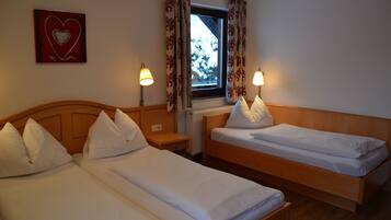 Een hotelkamer met twee enkele bedden, een raam met gordijnen, een hartdecoratie aan de muur en twee bedlampjes.