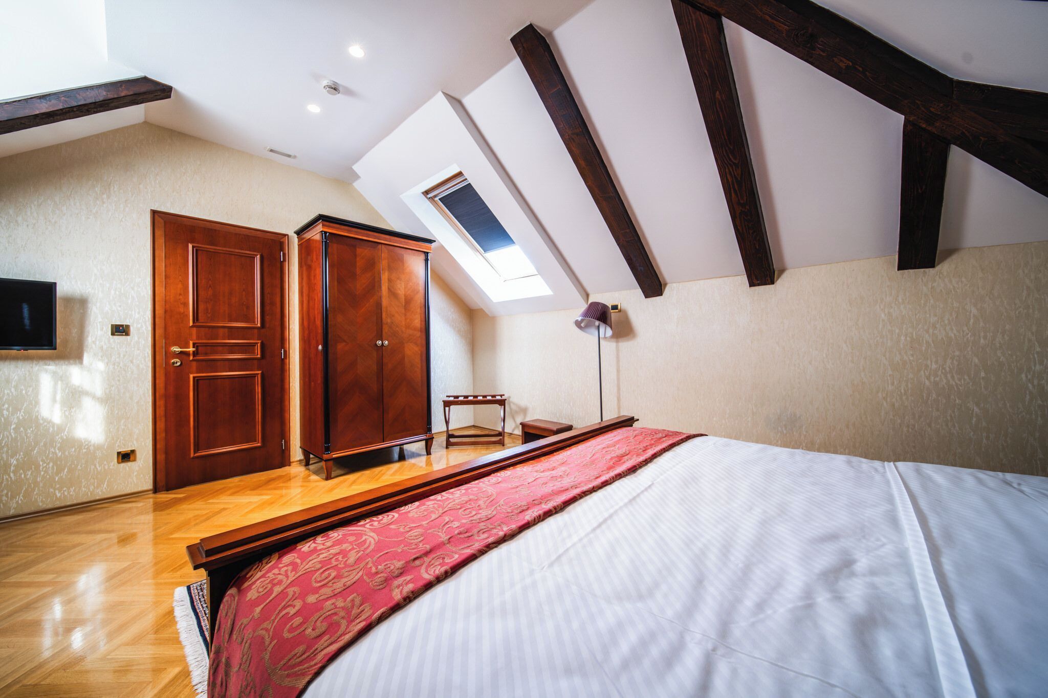A bedroom with a skylight, wooden wardrobe, and a bed with a red bedspread.