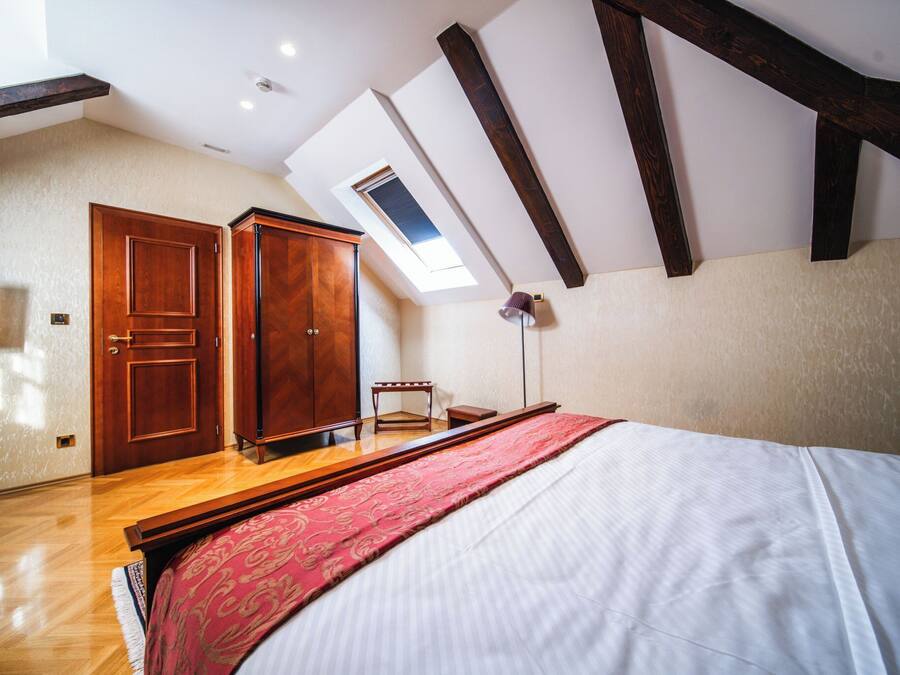 A bedroom with a skylight, wooden wardrobe, and a bed with a red bedspread.
