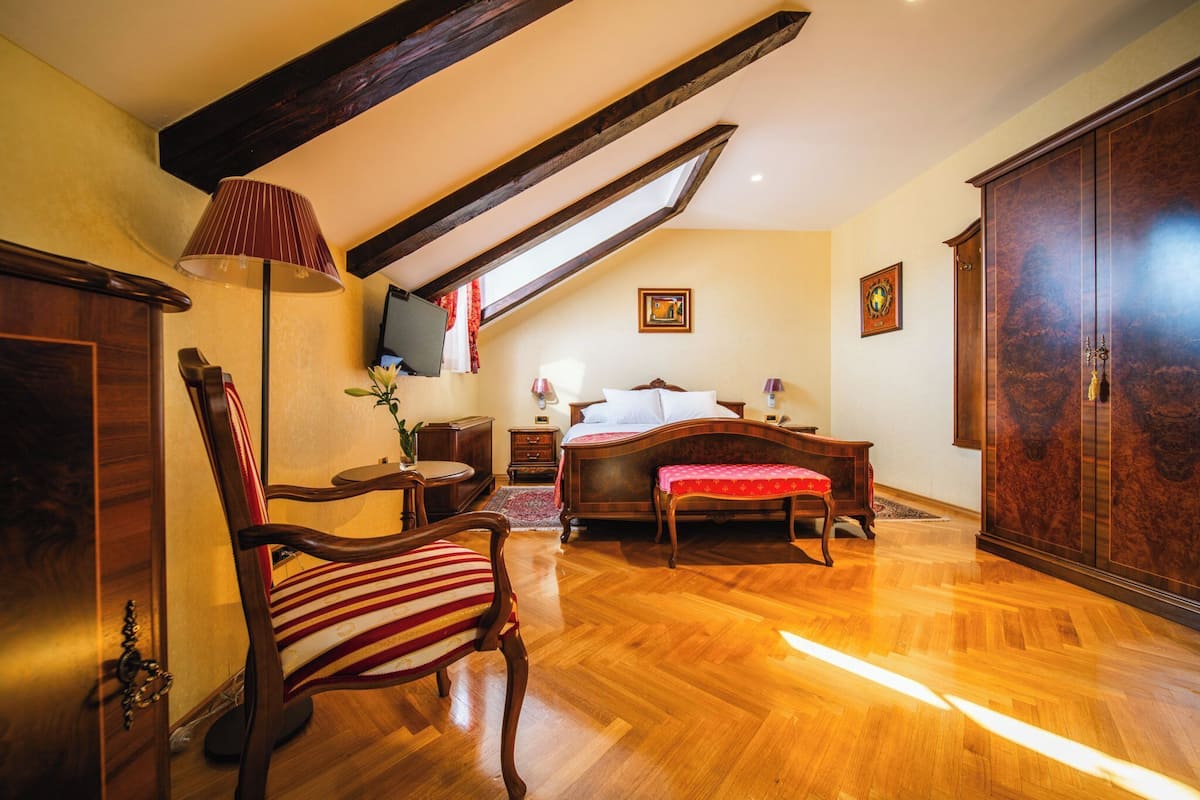 Ein Schlafzimmer mit Holzboden, einem Bett und einem rot-weiß gestreiften Sessel, einem Holzschrank sowie einem Fernseher an der Wand.
