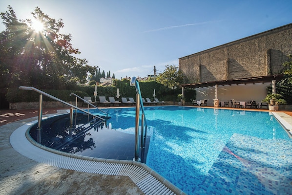 Une piscine avec une terrasse carrelée, des chaises longues et un bâtiment en pierre en arrière-plan.