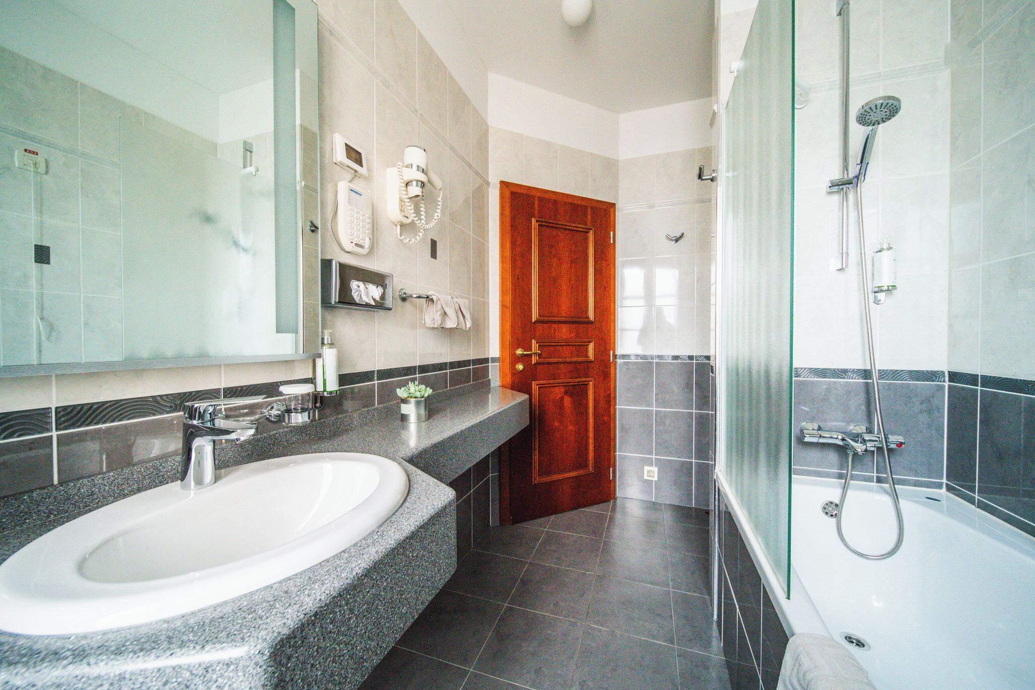 A modern bathroom with a granite countertop sink, a glass shower enclosure, and a wooden door.