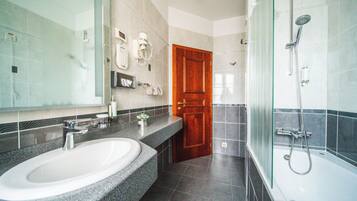 A modern bathroom with a granite countertop sink, a glass shower enclosure, and a wooden door.