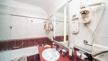 A modern bathroom with a white sink, red-tiled walls, a glass shower enclosure, a hairdryer, and a towel rack.