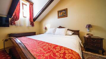 Quarto com uma cama grande, cabeceira de madeira, mesa de cabeceira com abajur, pequena mesa com um livro e um quadro na parede.