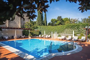 A swimming pool with lounge chairs and a pergola, surrounded by greenery and a stone wall.