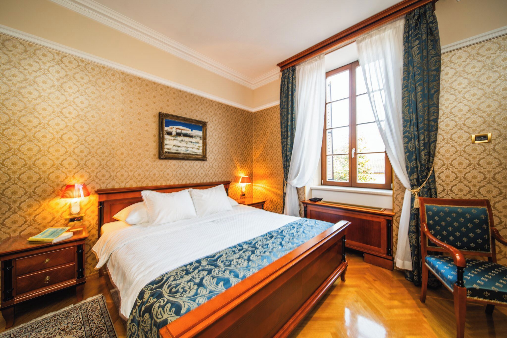 Une chambre d’hôtel avec un grand lit, deux lampes de chevet, une chaise, une fenêtre avec des rideaux et un tableau accroché au mur.