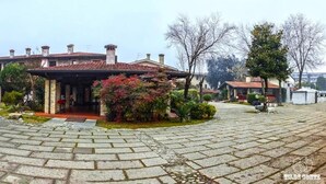 Una casa de dos pisos con techo de tejas, un porche delantero y un pequeño jardín con follaje rojo.