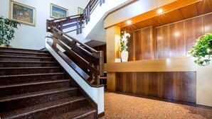 Una escalera con barandillas de madera que lleva a una recepción con un mostrador de madera y un jarrón de flores.