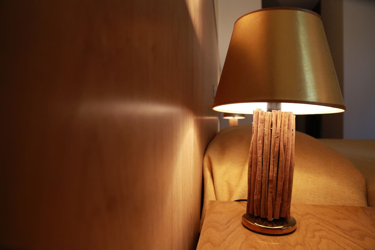 Een houten nachtkastje met een lamp met een cilindrische voet en een conische lampenkap.