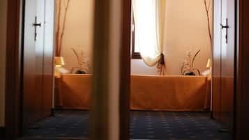Una habitación con cama, ventana con cortinas, lámpara y planta.