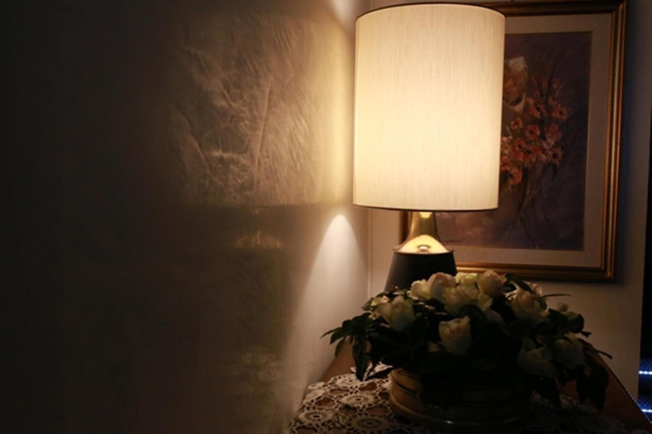 A lamp with a white shade on a table next to a framed painting.