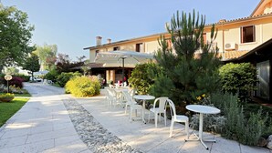 Un patio al aire libre con sillas y mesas blancas, un sendero y un edificio con tejado de azulejos.