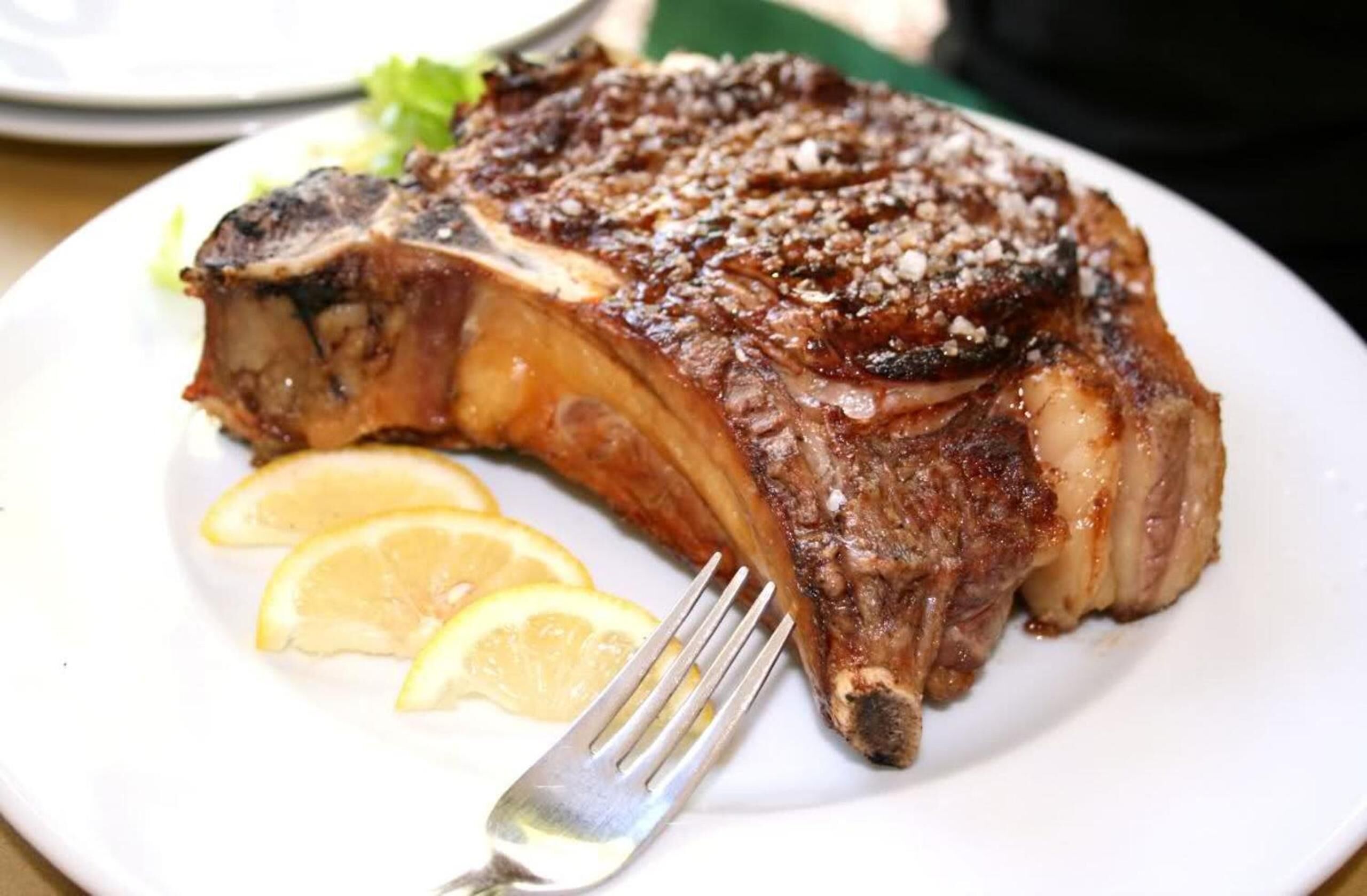 A steak with lemon slices on a white plate.