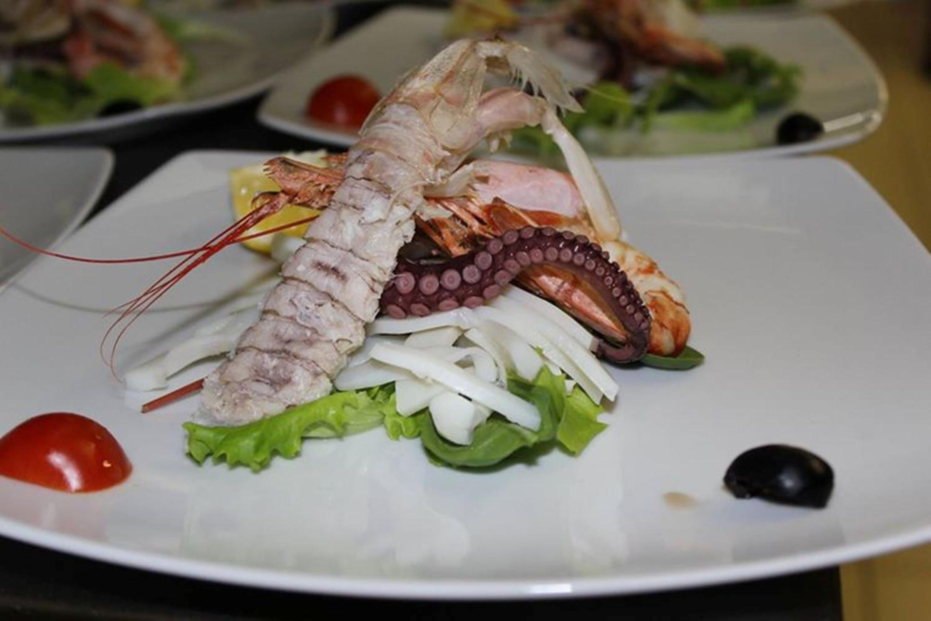 Un piatto con astice, polpo e verdure.