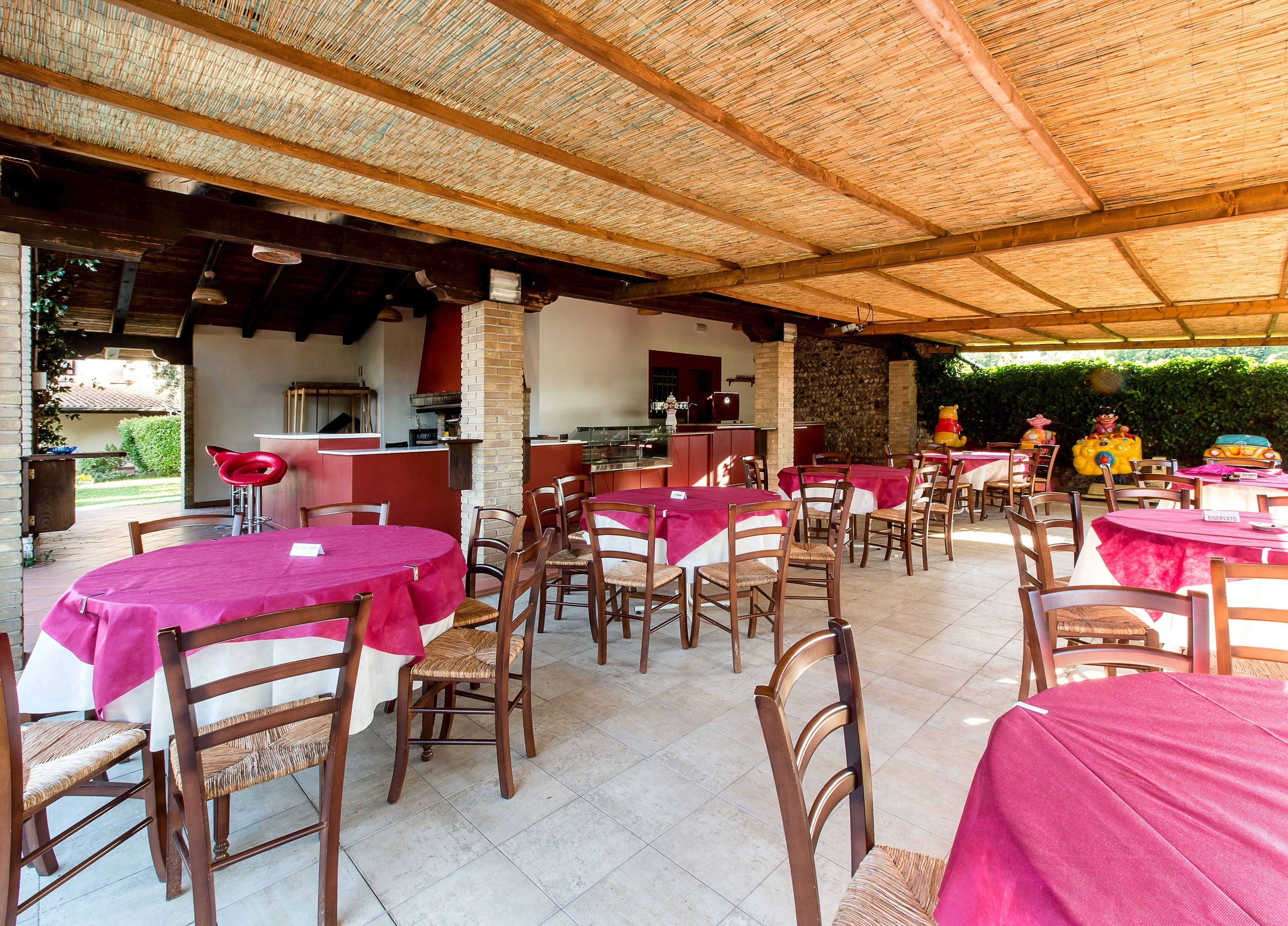 Een terras met ronde tafels, bedekt met roze tafelkleden en houten stoelen.