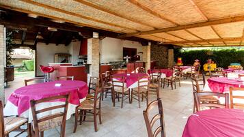 Een terras met ronde tafels, bedekt met roze tafelkleden en houten stoelen.