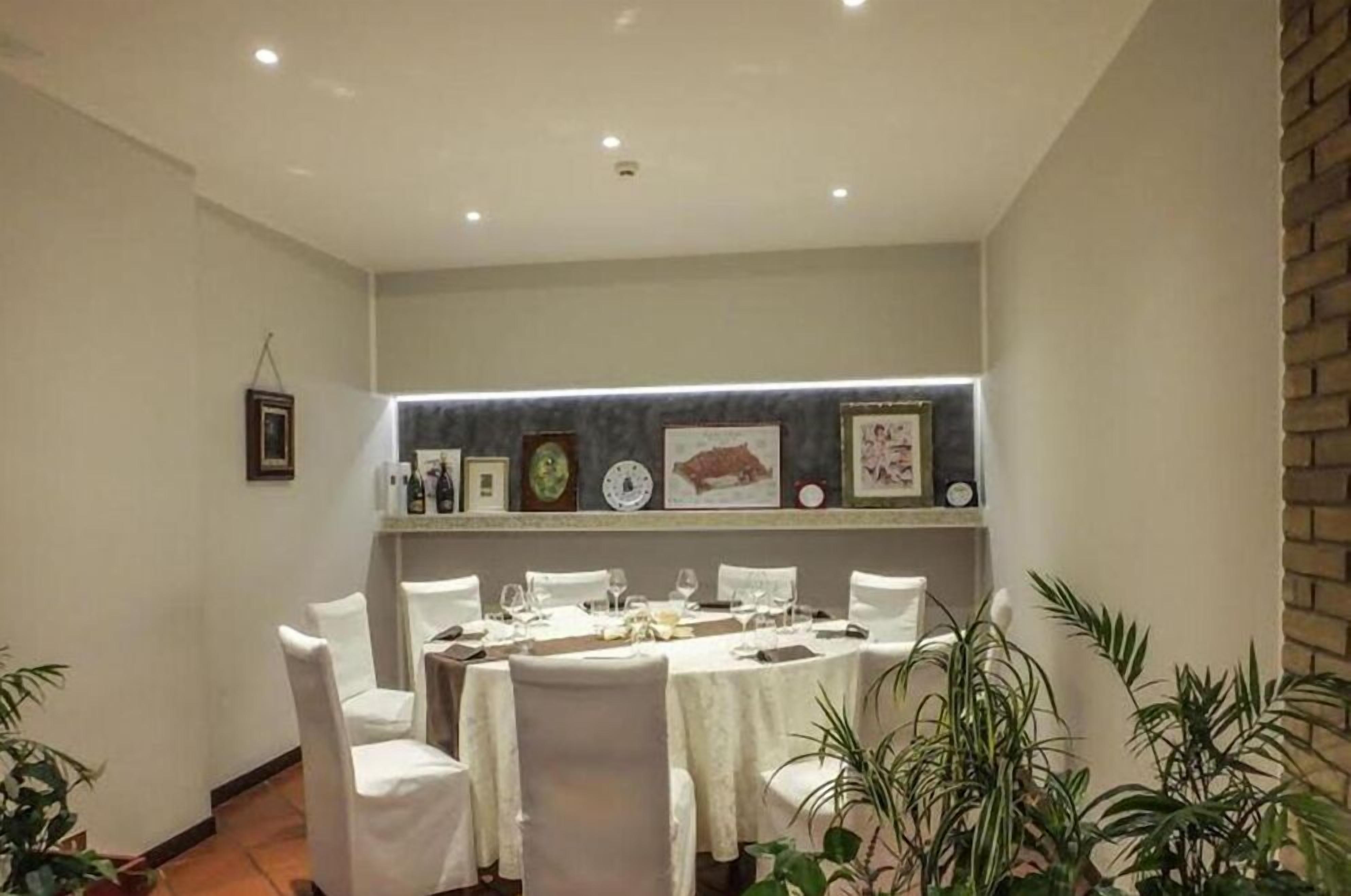 Un comedor con una mesa larga dispuesta para seis, sillas blancas y una pared decorada con cuadros y un reloj.