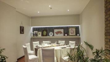 Un comedor con una mesa larga dispuesta para seis, sillas blancas y una pared decorada con cuadros y un reloj.