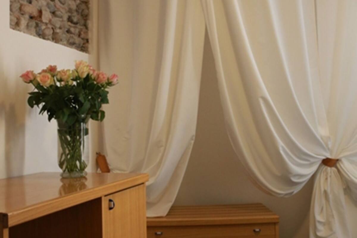 Een kamer met een houten bureau, een bloevas, een stenen muur en een gordijn.