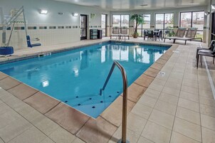 Una piscina interior con trampolín, sillas de descanso y suelo de baldosas.