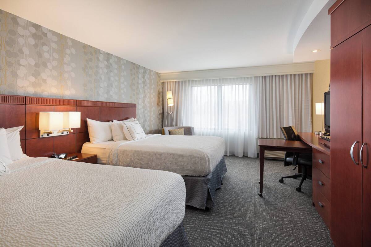 A hotel room with two beds, a desk, and a wardrobe.