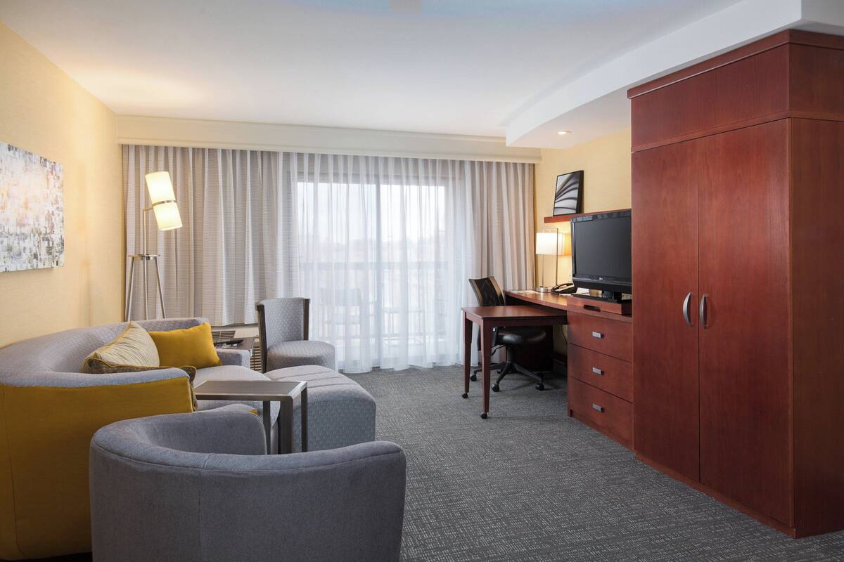 A hotel room with a sofa, armchair, desk, and TV.