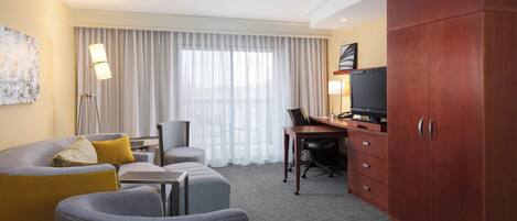 Quarto de hotel com sofá, poltrona, escrivaninha e televisão.
