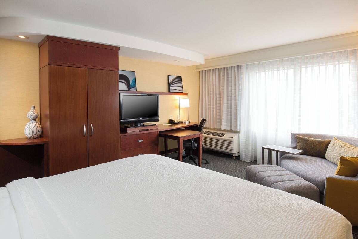 A hotel room with a large bed, a desk with a computer, a television, and a sofa.