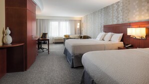 A hotel room with two beds, a desk, a chair, a lamp, and a large window with curtains.