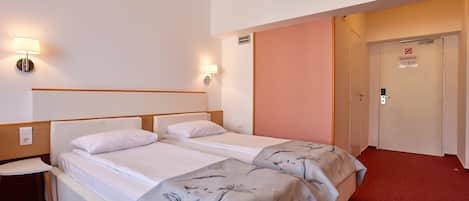 A hotel room with two beds, a nightstand, and a door with a sign.