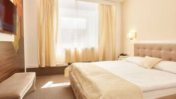 Quarto de hotel com uma cama grande, uma mesa de cabeceira, uma luminária e uma janela com cortinas.