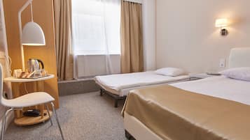Quarto de hotel com duas camas de solteiro, uma escrivaninha com cadeira, cafeteira e luminária.