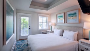 A hotel room with a large bed, two bedside tables, a ceiling fan, and two framed pictures on the wall. - Coco Plum Inn (Key West)