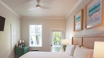 A bedroom with a bed, a ceiling fan, a window with blinds, a door, a green dresser, and framed artwork on the wall.