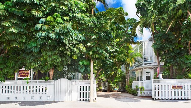 A gated entrance with lush green foliage and a white picket fence. - Coco Plum Inn (Key West)