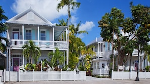 A white colonial-style building with a balcony, surrounded by palm trees and a white picket fence. - Coco Plum Inn (Key West)