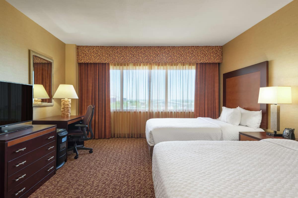 A hotel room with two beds, a desk with a television, and a chair.