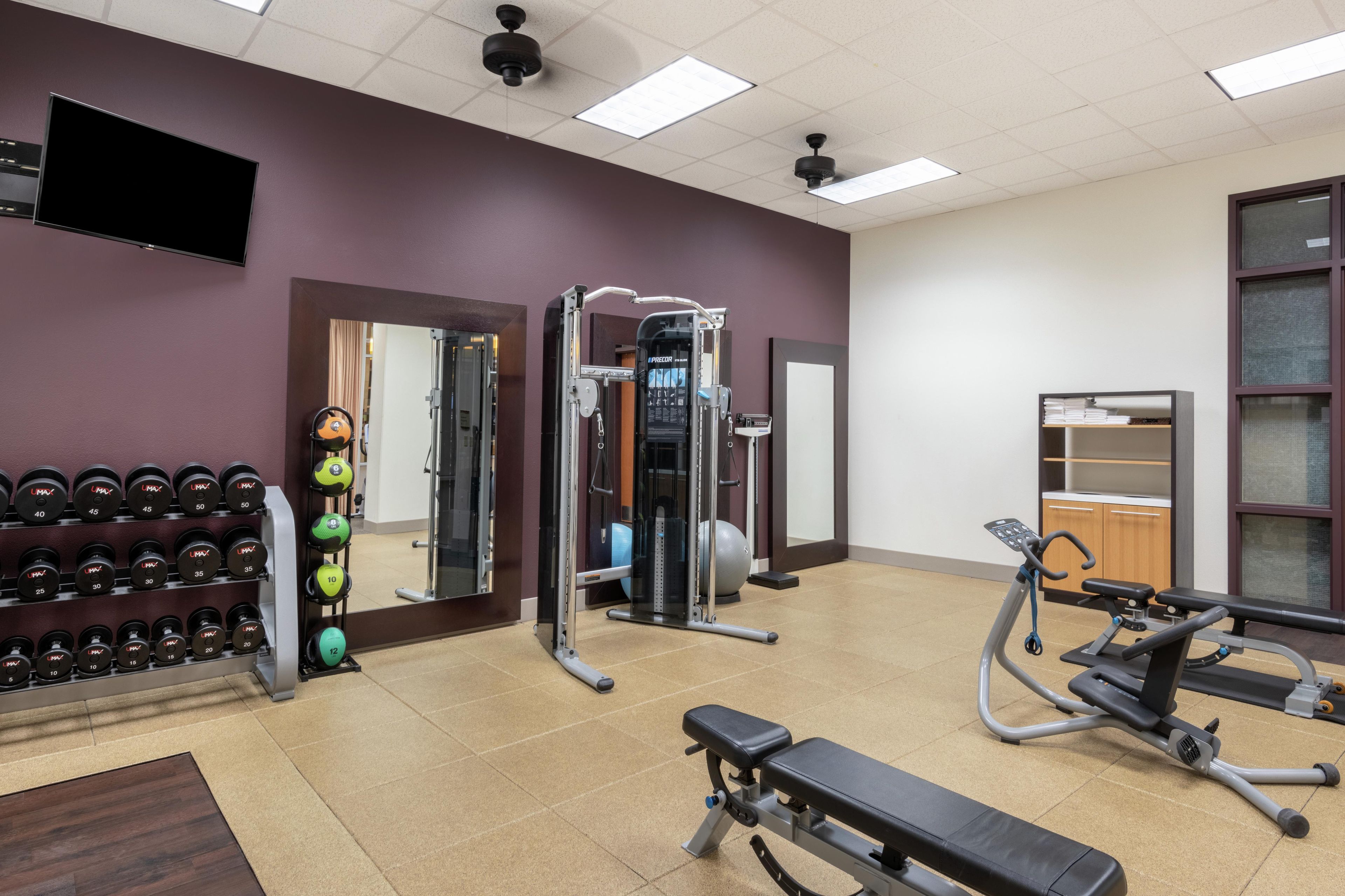 Une salle de sport équipée de matériel d’exercice, d’un banc et d’un téléviseur fixé au mur.