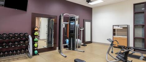 A gym with exercise equipment, a bench, and a wall-mounted TV.