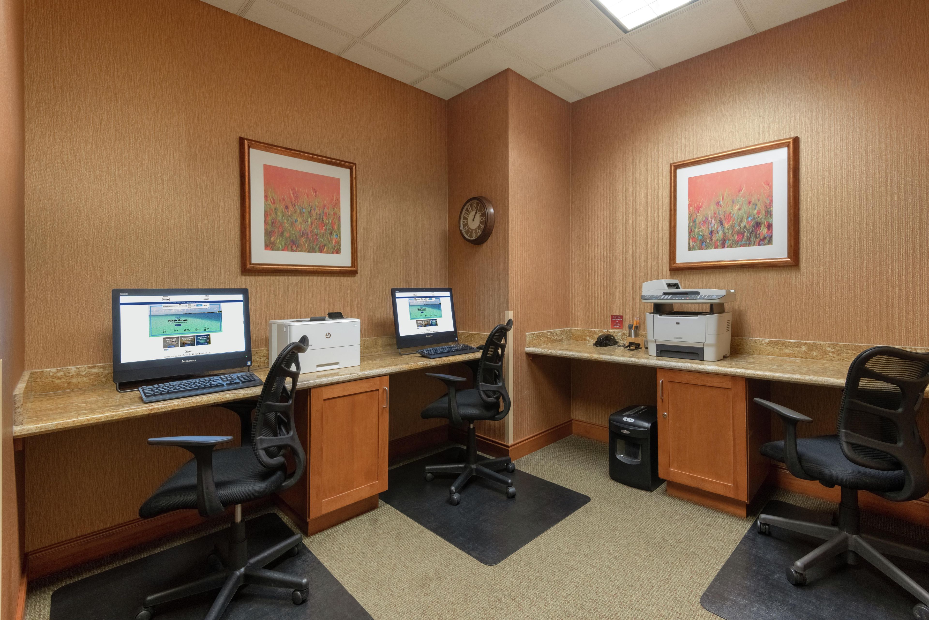 Ein Hotelbüro mit zwei Schreibtischen, Computern, Stühlen, einem Drucker und gerahmten Kunstwerken an den Wänden.