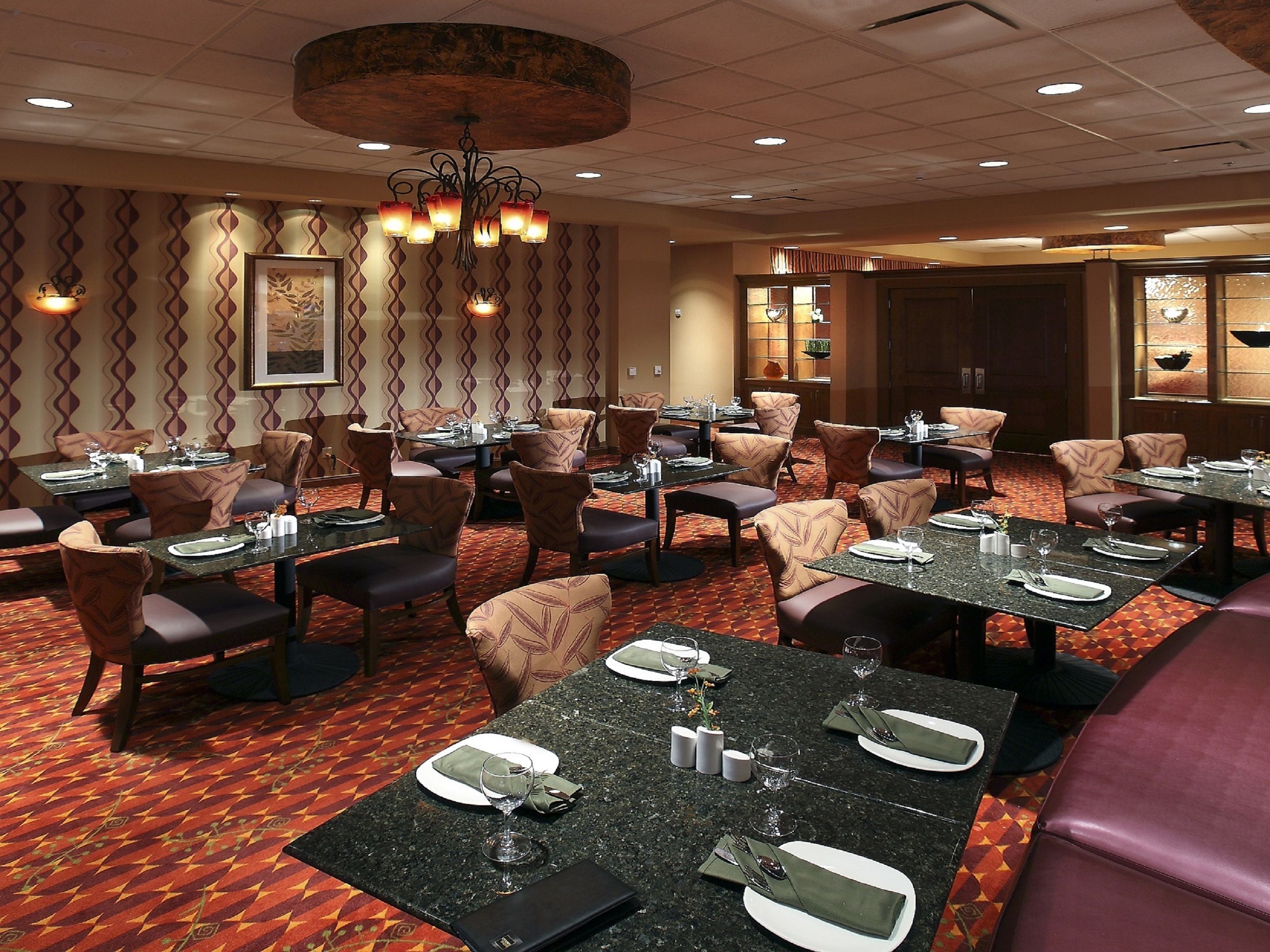 A restaurant with multiple tables and chairs, a patterned carpet, and a chandelier.