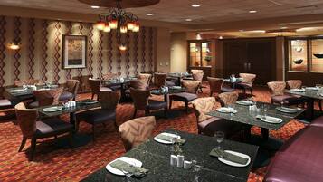 A restaurant with multiple tables and chairs, a patterned carpet, and a chandelier.
