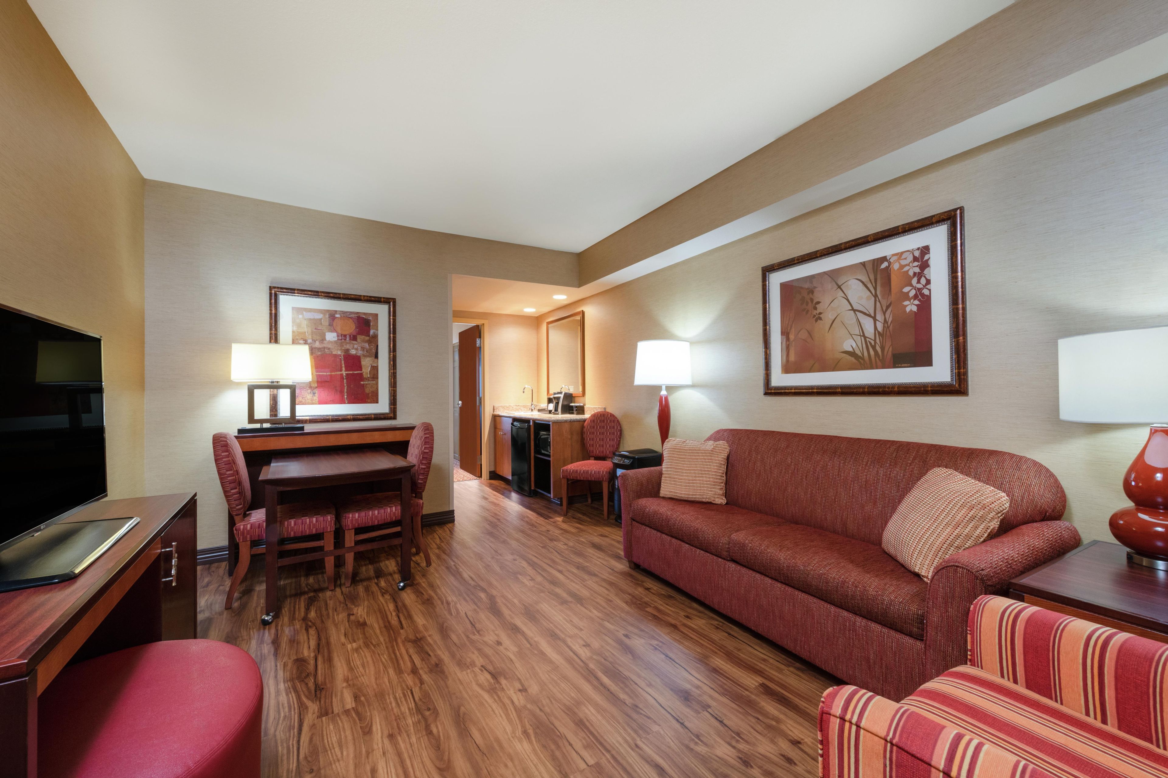 A hotel room with a dining area, a sofa, a TV, and a kitchen area.