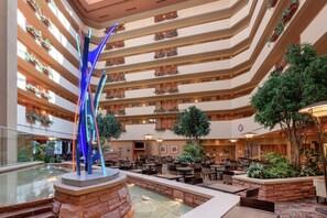 A multi-level hotel atrium with a central water feature, multiple dining areas, and balconies with plants. - Embassy Suites by Hilton Loveland Conference Center (Loveland)