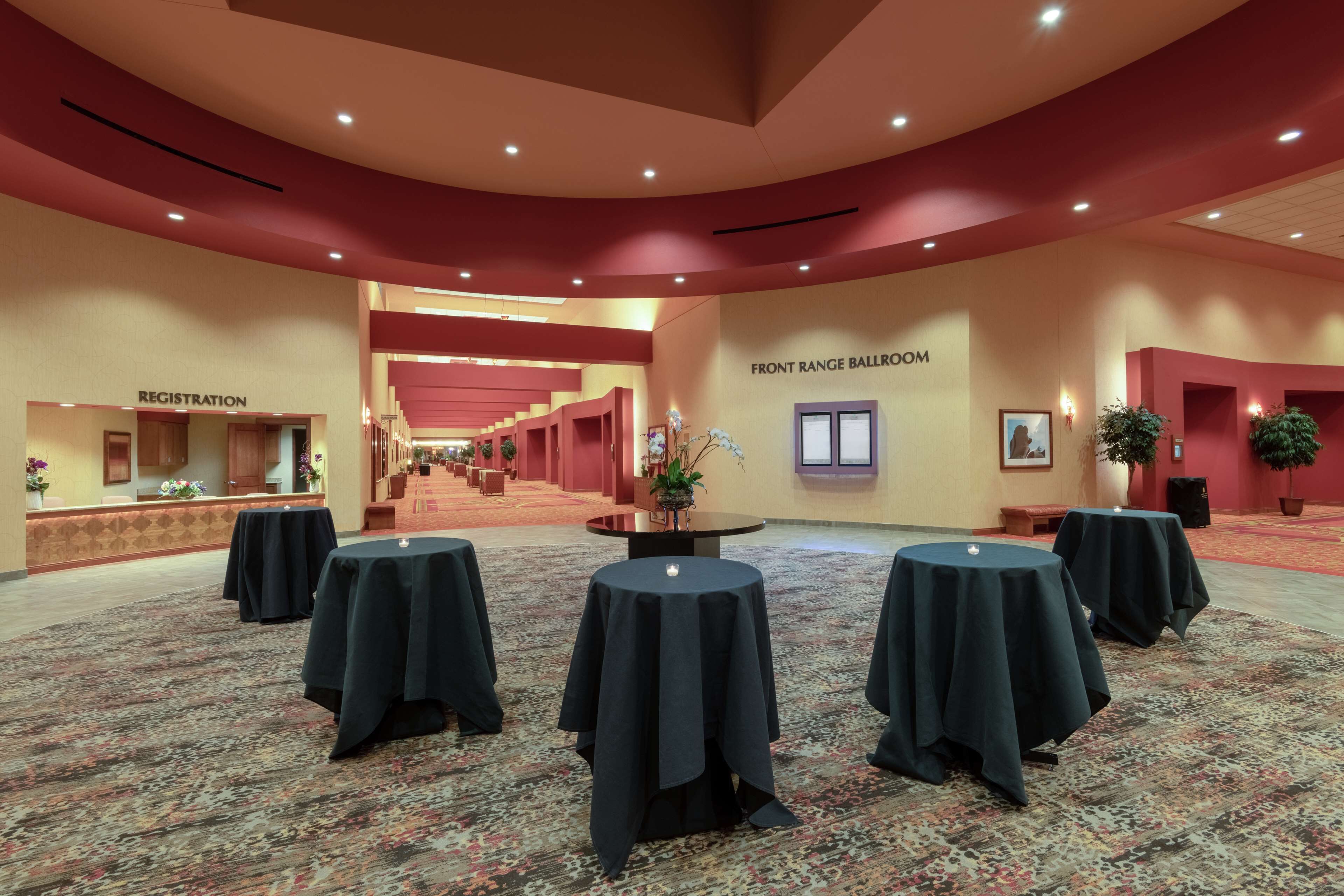 A spacious hall with a registration area, a front range ballroom, and multiple round tables covered with tablecloths.