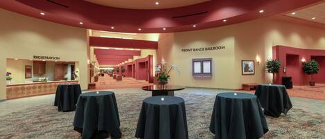 A spacious hall with a registration area, a front range ballroom, and multiple round tables covered with tablecloths.