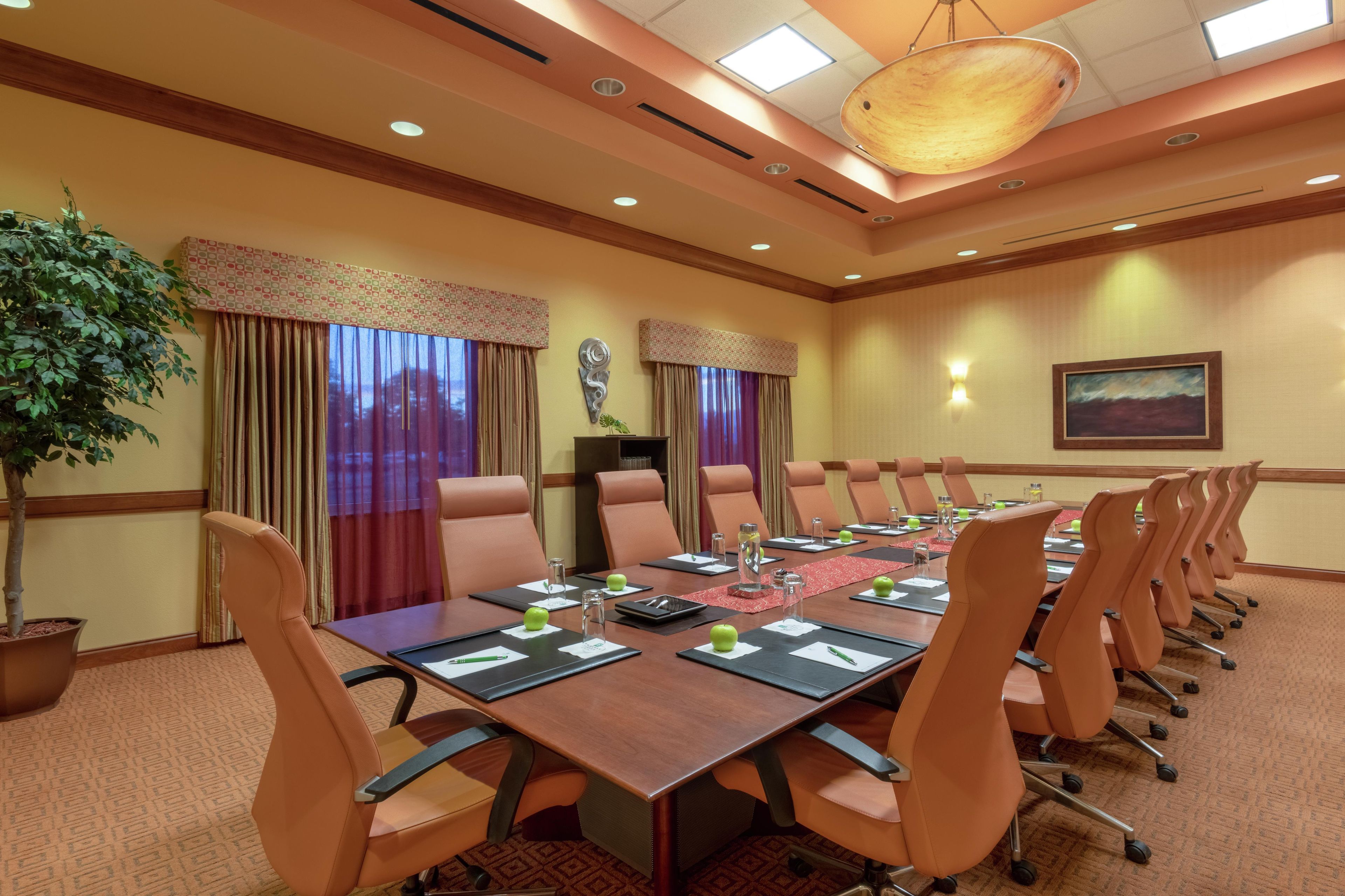 A conference room with a long table, multiple chairs, a potted plant, and a painting on the wall.